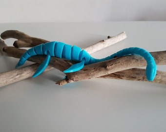 Puede incluir: Un dinosaurio de plástico azul brillante, que se asemeja a un plesiosaurio, está posado sobre un conjunto de ramas de madera flotante.