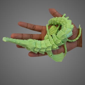 May include: A green 3D printed seahorse necklace. The seahorse is curled up and has a detailed design.