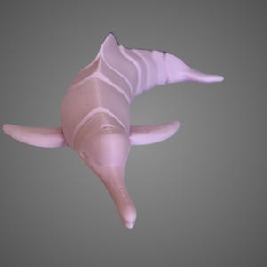 May include: A pink 3D printed dolphin figurine. The dolphin is posed in a swimming position with its head tilted up and its mouth closed. The figurine is made of a smooth, plastic-like material.