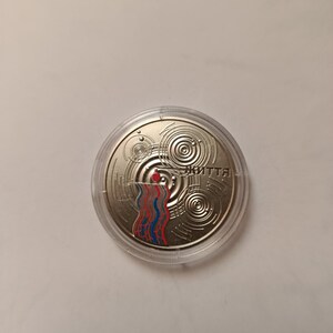 May include: A silver coin encased in a clear plastic holder. The coin features concentric circles and a colorful design of red, blue, and white vertical lines. The word "життя" is printed on the coin.