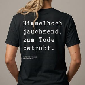 Könnte beinhalten: Schwarzes T-Shirt mit weißem Text auf dem Rücken. Der Text lautet "Himmelhoch jauchzend, zum Tode betrübt." Darunter steht "Klärchens Lied, 1788 J.W. von Goethe."