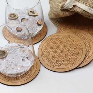 Könnte beinhalten: Satz mit sechs Untersetzern aus Holz mit einem geometrischen Lebensblume-Design. Die Untersetzer sind hellbraun und haben eine natürliche Holzoptik. Die Untersetzer sind übereinander gestapelt und liegen auf einer weißen Oberfläche.