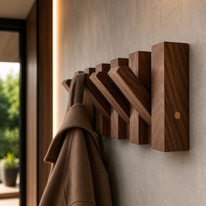 Könnte beinhalten: Ein hölzerner, an der Wand befestigter Kleiderhaken mit sechs abgewinkelten Haken. Der Haken besteht aus dunkelbraunem Holz und ist an einer hellgrauen Wand befestigt. Ein brauner Mantel hängt an einem der Haken. Das Design ist modern und minimalistisch.