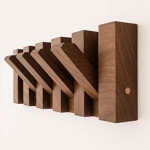 Puede incluir: Un perchero de pared de madera con una serie de ganchos angulados. El perchero es de madera marrón oscuro y tiene un diseño moderno y geométrico. Los ganchos miden aproximadamente 15 cm de largo. Un pequeño acento redondo de color cobre es visible en el lado derecho.