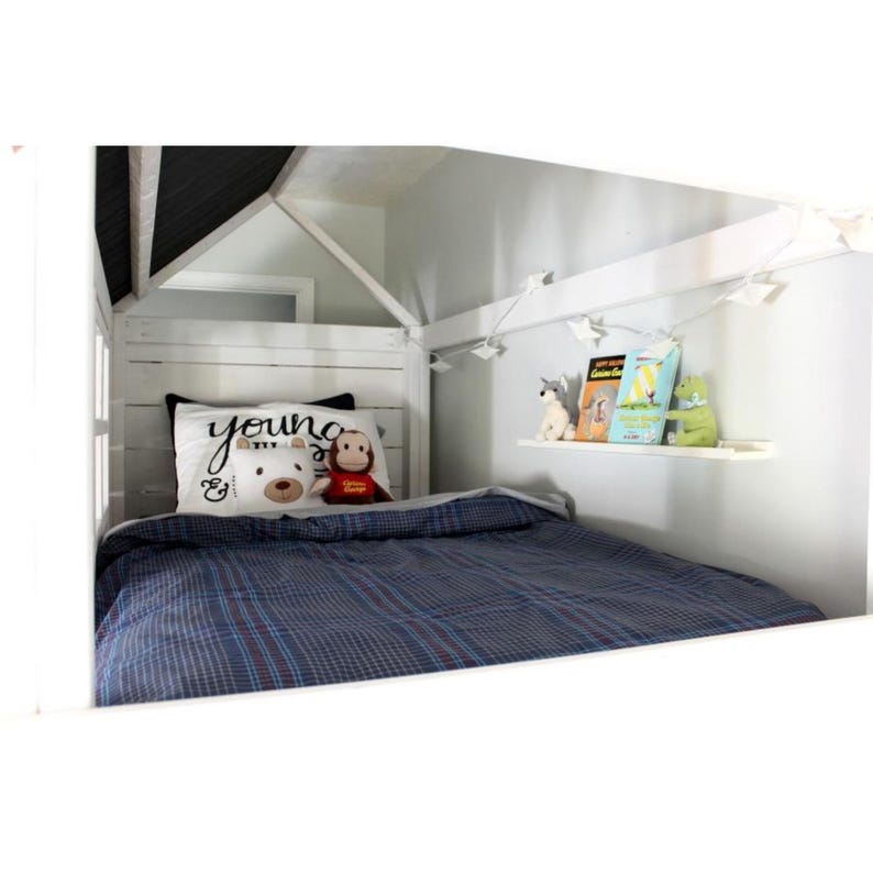 May include: A white wooden house-shaped bed frame with a blue plaid blanket. A pillow with the word "young" and a teddy bear and monkey plush toys are on the bed. A shelf holds books and stuffed animals.