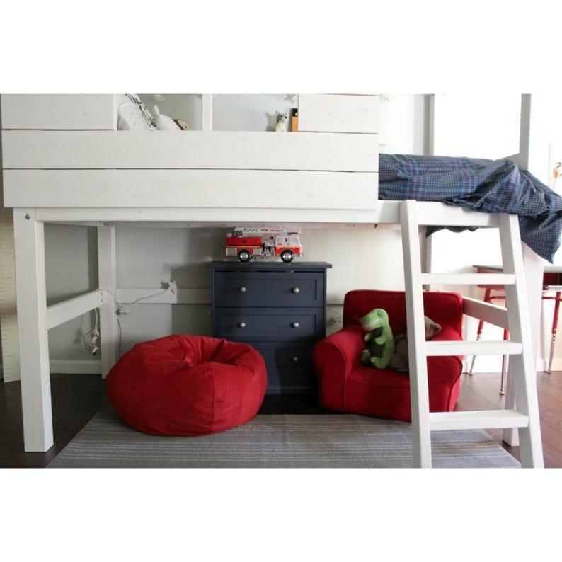 May include: A white loft bed with a built-in ladder, over a red beanbag chair, a red armchair, and a navy blue dresser. A toy fire truck sits on the dresser. A green stuffed dinosaur is in the armchair. The bed has a blue plaid blanket.