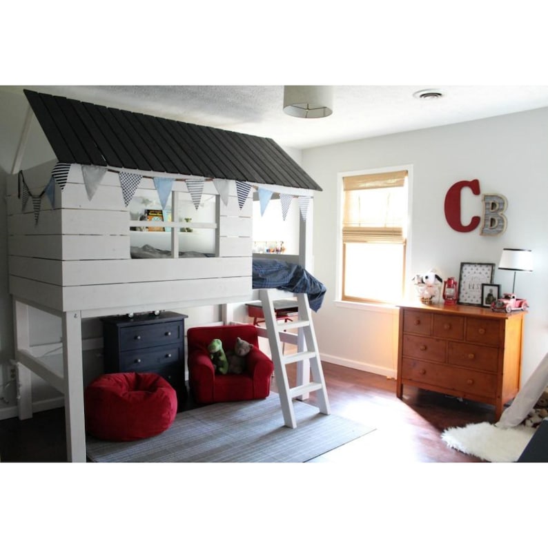 May include: A white loft bed with a black roof, designed to resemble a house. The bed has a ladder for access and is decorated with blue and white pennant flags. A red beanbag chair and a red armchair are placed below the bed.