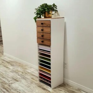 May include: White cabinet with four wooden drawers and a shelf unit with multiple compartments. The cabinet is filled with colorful paper.