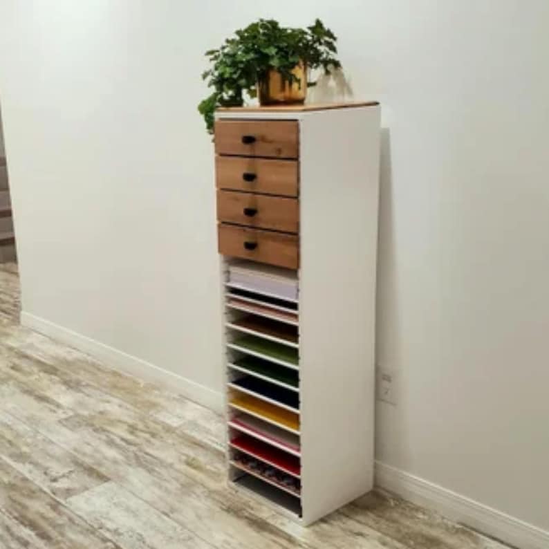 May include: White cabinet with four wooden drawers and a shelf unit with multiple compartments. The cabinet is filled with colorful paper.