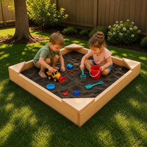 May include: A wooden sandbox filled with dark sand, featuring two children playing with colorful toys. The sandbox is square with triangular corner seats. Toys include a yellow and red toy truck, a red bucket, and blue and green shovels.