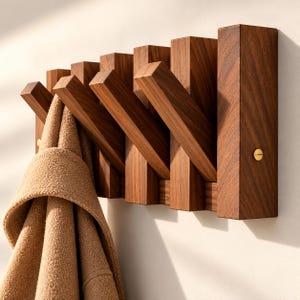 May include: A wall-mounted coat rack made of dark brown wood with five angled, retractable hooks. The rack features a rectangular base with visible wood grain and two brass-coloured screws on the sides. A tan textured coat hangs from one hook.