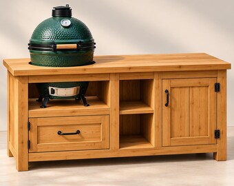 May include: A dark green ceramic kamado-style grill with a silver temperature gauge and a light wood handle, set into a rectangular light brown wooden outdoor kitchen island featuring one drawer, two open shelves, and a single cabinet door.