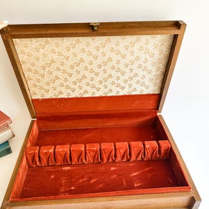 May include: Open wooden silverware box with a red velvet interior and a floral patterned lid lining. The box has slots for utensils and a brass clasp. The exterior is a warm brown color.