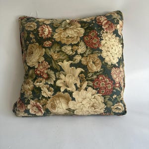 K&ouml;nnte beinhalten: Quadratisches Zierkissen mit dunkelgr&uuml;nem Hintergrund und gro&szlig;em Blumenmuster. Die Blumen sind in Creme-, Rot- und Gelbt&ouml;nen gehalten. Das Kissen hat ein weiches, strukturiertes Aussehen, was auf ein komfortables Design hindeutet.