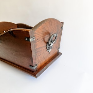 May include: A dark brown wooden box with a curved top and a decorative metal handle. The box has metal corner brackets and a rectangular base. The wood grain is visible, and the box appears to be vintage.