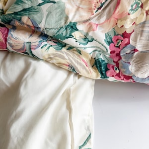 May include: A floral patterned comforter with a white pillowcase. The comforter features large, soft pink, yellow, and red flowers with green leaves on a white background. The pillowcase is a solid, off-white color.