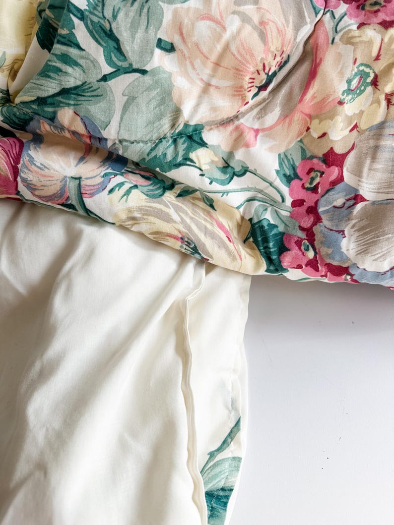 May include: A floral patterned comforter with a white pillowcase. The comforter features large, soft pink, yellow, and red flowers with green leaves on a white background. The pillowcase is a solid, off-white color.
