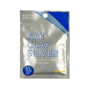 Könnte beinhalten: Eine silberne Verpackung von Art Clay Silver, einem Bastelmaterial. Die Verpackung hat ein blau-weißes Design und den Text "ART CLAY SILVER". Sie gibt an, dass der Inhalt 10g Silberton Ag 92% beträgt. Es gibt auch japanischen Text.