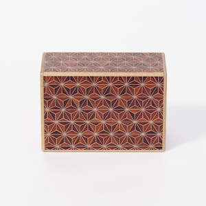 Può includere: Una scatola rettangolare in legno caratterizzata da un complesso motivo geometrico a intarsio sulle superfici superiore e frontale. Il design è composto da forme ripetute di stelle e triangoli in varie tonalità di legno marrone, scuro e chiaro.