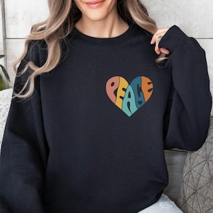 May include: A black sweatshirt with a rainbow heart graphic that says "PEACE" inside. The heart is centered on the chest of the sweatshirt.
