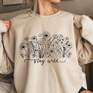 May include: A beige sweatshirt with a black floral design and the text "stay wild" printed on the front.