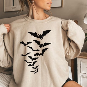 May include: A beige sweatshirt with a black silhouette of a flock of bats printed on the front.