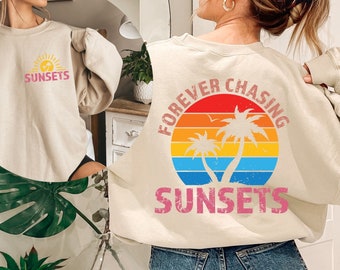 May include: A beige sweatshirt with a graphic print of a sunset and palm trees. The text "FOREVER CHASING SUNSETS" is printed on the sweatshirt.