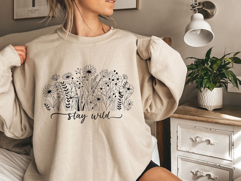 May include: A beige sweatshirt with a black floral design and the text "stay wild" printed on the front.