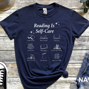 May include: Navy blue t-shirt with white text that reads "Reading Is Self-Care" and illustrations of books with text describing the benefits of reading.