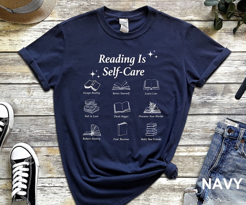 May include: Navy blue t-shirt with white text that reads "Reading Is Self-Care" and illustrations of books with text describing the benefits of reading.