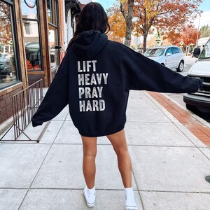 May include: Black hooded sweatshirt with the text "LIFT HEAVY PRAY HARD" printed on the back in white.