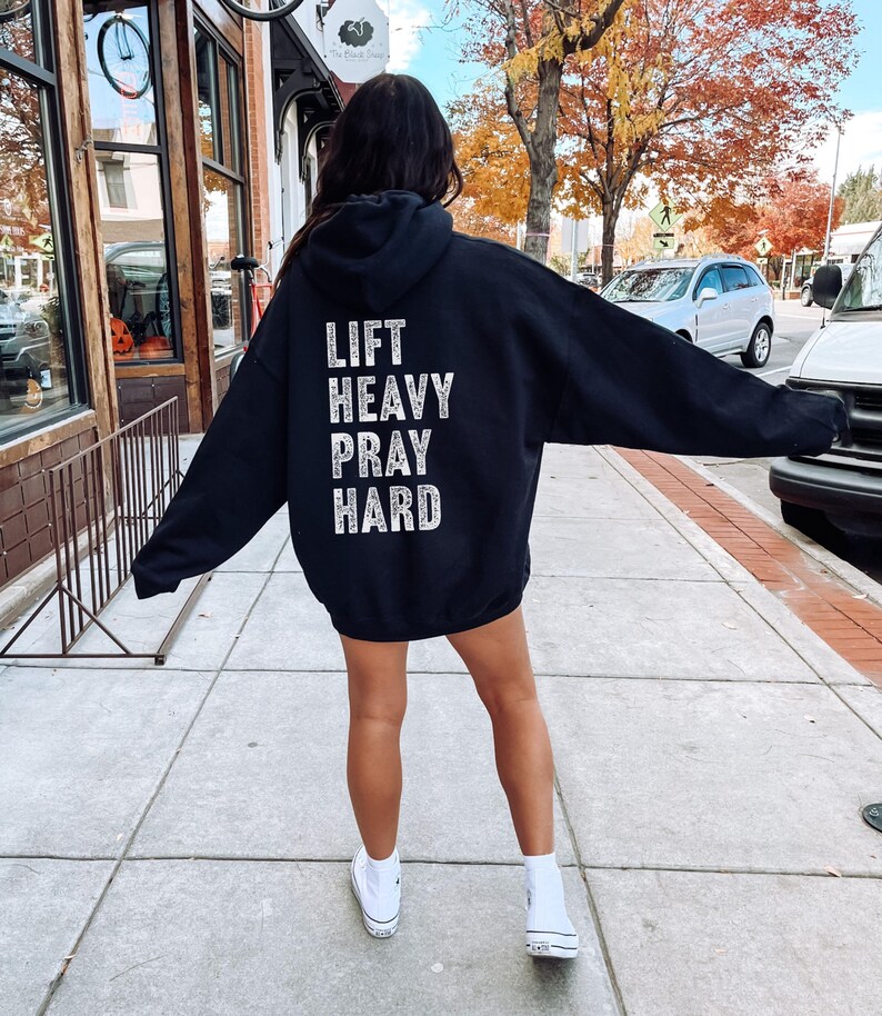 May include: Black hooded sweatshirt with the text "LIFT HEAVY PRAY HARD" printed on the back in white.