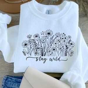 May include: White sweatshirt with a black floral design and the text "stay wild" printed on the front.