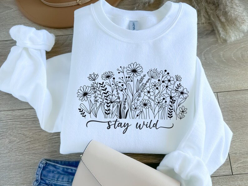 May include: White sweatshirt with a black floral design and the text "stay wild" printed on the front.