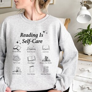 May include: Gray sweatshirt with the text "Reading Is Self-Care" and illustrations of books with phrases like "Escape Reality", "Better Yourself", "Learn Lots", "Fall in Love", "Think Bigger", "Discover New Worlds", "Reduce Anxiety", "Find Passions", and "Make New Friends".