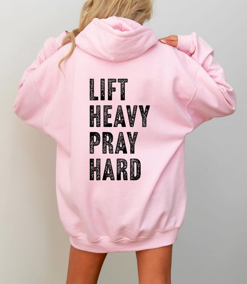 May include: A pink hoodie with the text "LIFT HEAVY PRAY HARD" printed on the back in black.