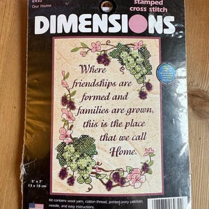 May include: A Dimensions stamped cross stitch kit with the text "Where friendships are formed and families are grown, this is the place that we call Home." The kit includes wool yarn, cotton thread, and a needle. The dimensions are 13 x 18 cm.