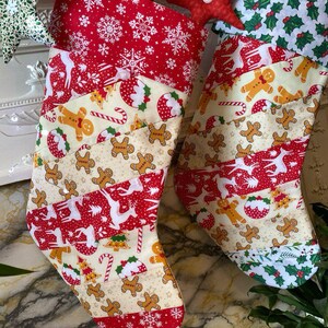 May include: Two Christmas stockings with festive patterns. One stocking features red fabric with white snowflakes, reindeer, and gingerbread men. The other stocking has a similar design with holly and gingerbread men. The stockings are decorated with star-shaped ornaments.