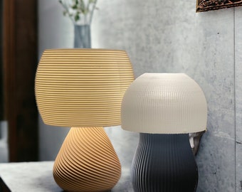 Könnte beinhalten: Zwei moderne Tischlampen im Pilz-Design. Die Lampe links hat einen beigefarbenen Schirm und einen Holzfuß mit einem Spiralmuster. Die Lampe rechts hat einen weißen Schirm und einen schwarzen Fuß mit einem ähnlichen Spiralmuster.