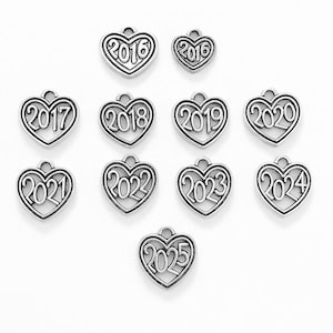 May include: Silver-toned heart-shaped charms with years 2016 through 2025. Each charm has a loop at the top for attaching to a chain or bracelet. The numbers are in a stylized font within the heart outline.