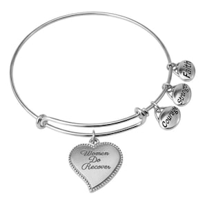 May include: A silver-colored bangle bracelet with a heart-shaped charm that reads "Women Do Recover." The bracelet also features three small charms with the words "Courage," "Strength," and "Faith."