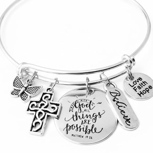 May include: Silver-toned bangle bracelet with multiple charms. Charms include a butterfly, a cross, a round charm with the text "With God all things are possible", a rectangular charm with the word "Believe", and a round charm with the words "Love Faith Hope".