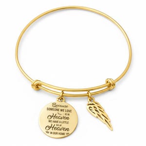 Può includere: Bracciale dorato con due ciondoli. Un ciondolo è un ciondolo rotondo con il testo "Because someone we love is in Heaven we have a little bit of Heaven in our home." L'altro ciondolo è un'ala.