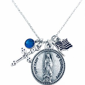 Peut inclure: Collier argenté avec une croix, une pierre bleue, un médaillon de Notre-Dame de Guadalupe et un petit drapeau américain. La chaîne est fine et les breloques sont détaillées.