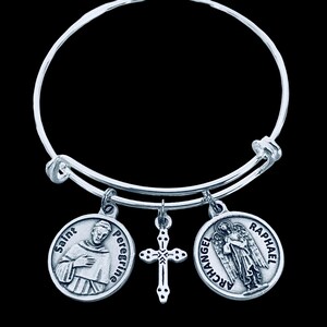 May include: Silver-toned bangle bracelet with three charms. The charms include a cross pendant and two round medallions. One medallion features Saint Peregrine, and the other depicts Archangel Raphael.