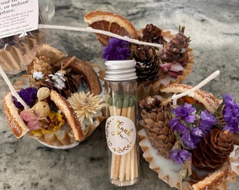 Könnte beinhalten: Dekorative Feueranzünder mit getrockneten Blumen, Tannenzapfen und Orangenscheiben. Ein kleines Glasfläschchen mit Streichhölzern und einem "Thank You"-Aufkleber befindet sich in der Mitte.
