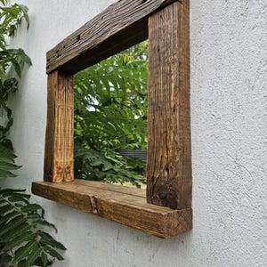 May include: A rustic wooden mirror with a shelf underneath. The mirror is rectangular and has a dark brown finish. The shelf is made of the same wood as the frame and is also dark brown.