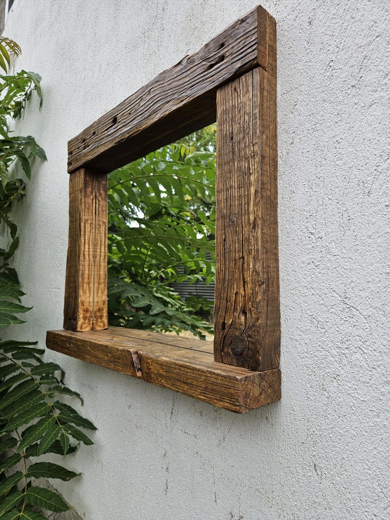 May include: A rustic wooden mirror with a shelf underneath. The mirror is rectangular and has a dark brown finish. The shelf is made of the same wood as the frame and is also dark brown.