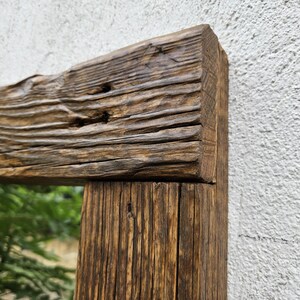 May include: A rustic wooden mirror frame with a natural wood finish. The frame is made of reclaimed wood with knots and grain patterns. The mirror is rectangular and has a clear reflection.