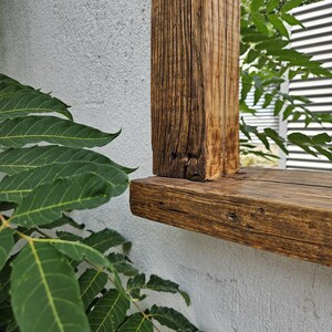 May include: Close-up of a wooden frame with a weathered, brown finish. The frame is mounted to a white wall and has a thick, horizontal top piece.